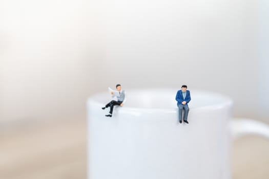 Two businessman miniature figure people standing on top of white mug cup of hot coffee with social distancing.