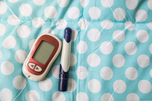 Close up of Glucose meter with lancet on light blue and white dot bed in bedroom on the morning using as Medicine, diabetes, glycemia, health care and people concept.