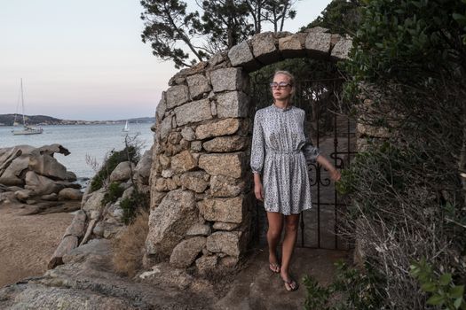 Beautiful woman in luxury summer dress enjoying peaceful seascape of Porto Rafael bay at Mediterranean sea of Costa Smeralda, Sardinia, Italy at dusk.