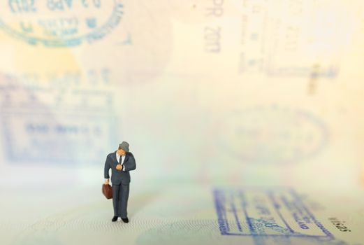 Time, Travel and planning concept. Businessman miniature figure people with suitcase standing and look to wrist watch on passport with immigration stamped and copy space.