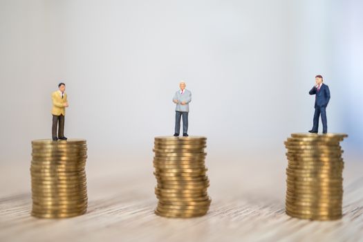 Business, Social Distancing Coronavirus, Covid-19 Protection Concept.  Three businessman miniature figure people standing on stack of gold coins on wooden table.