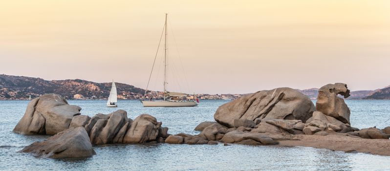 Sailboat sailing by beautiful rocky formations on the Spiaggia di Punta Nera beach. Luxury summer adventure, active vacation in Mediterranean sea, Costa Smeralda, Sardinia, Italy.