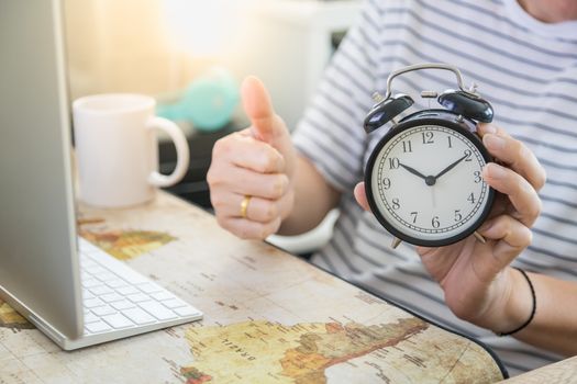 Business, Time, Technology, Work from home, Shelter in place Concept. Man hand holding vintage alarm clock with thumb up with desktop computer and white mug cup of coffee in his house.