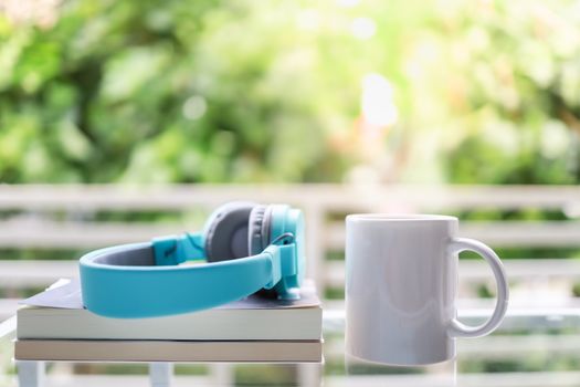 Hobby, Relaxation and Recreation Concept. Close up of white mug cup of hot coffee with headphone and books in garden with copy space.