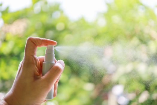 Health Care, Sanitary , Corona Virus (COVID-19) and Germ Protection Concept. Close up of man hand holding and spraying a mini bottle of alcohol 70% spray with green nature background and copy space.