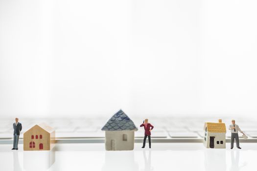 Business, Technology, Shelter in Place, Stay and Work from home and Social Distancing Concept for Coronavirus 2019 (COVID-19).  Three businessman miniature figure people standing and working with mini house toy  and computer keyboard and copy space.