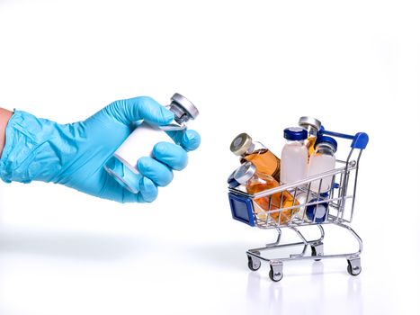 hand with blue latex glove holding medical vial with solution for injection and syringe ,and many medical vials in shopping cart, on white background.Vaccine trails for covid-19, can be affordable and accessible.