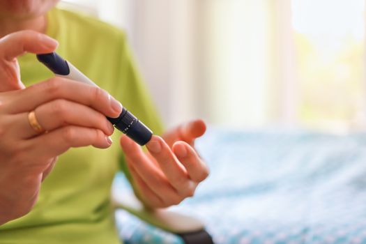 Close up of man hands using lancet on finger to check blood sugar level by Glucose meter in bedroom on the morning. Use as Medicine, diabetes, glycemia, health care and people concept.