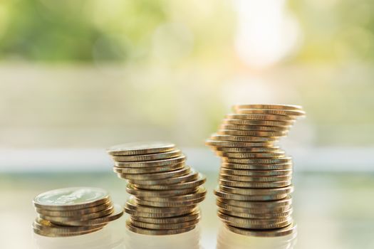 Business, Money, Finance, Security and Saving Concept. Close up of unstable stack of gold coins on table under sunlight and green nature background with copy space.