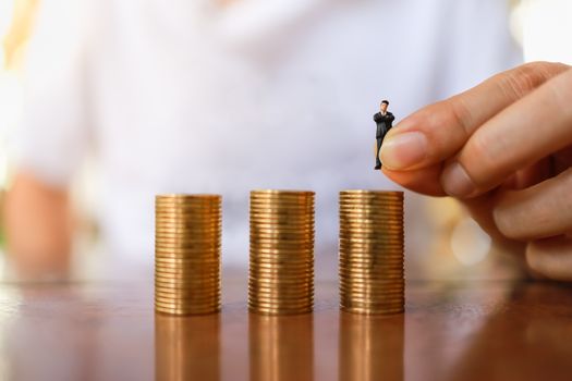 Business, Management and Human Resource Concept. Close up of man hand holding businessman miniature figure people and putting to top of stack of gold coins.