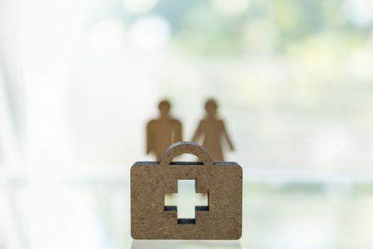 Healthcare,  Coronavirus (COVID-19) situation Cocept. Close up of wooden doctor bag with cross icon on table with man and woman model in blackground with copy space.