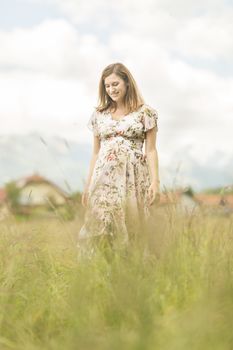 Portrait of beautiful pregnant woman in white summer dress relaxing in meadow full of yellow blooming flowers. Concept of healthy maternity care.