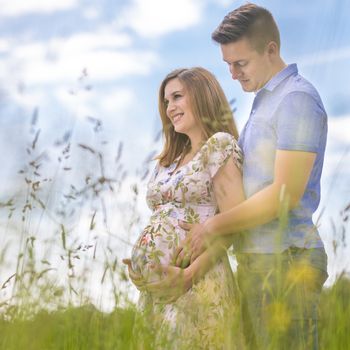 Young happy pregnant couple hugging in nature. Concept of love, relationship, care, marriage, family creation, pregnancy and parenting.