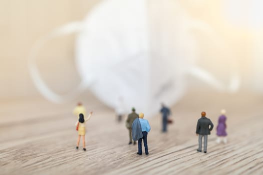 Healthcare, Coronavirus, Covid-19 Protection and Social Distancing  Concept. Group of businessman and woman miniature figure people standing and walking to N95 face mask on wooden table.