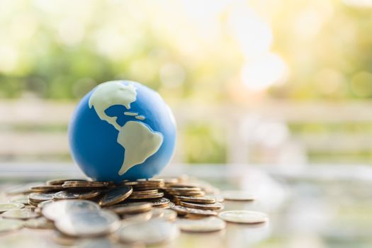 Global Business and Financial, Economic and palnning Concept. Close up of mini world ball on pile of gold coins with green nature background and copy space.