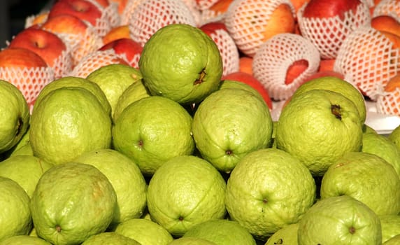 Fresh green guavas and apples for sale at an outdoor market
