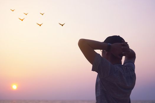 Man rise hands up to sky looking at birds fly through metaphor freedom concept with sunset sky and summer beach background.