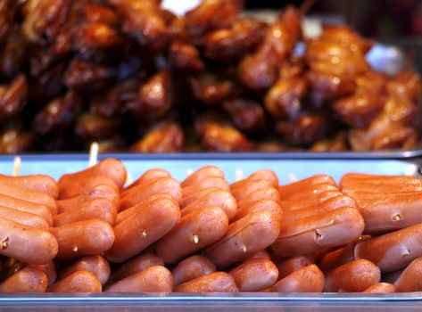 A market stall sells roasted hot dogs and fried chicken pieces