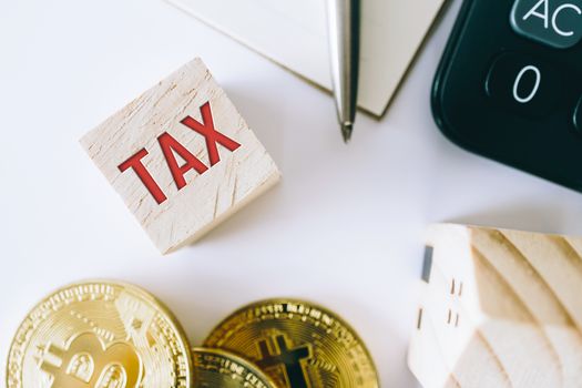 Tax word on wooden cube with objects as gold coin, calculator and mini home model behide white clean background. Business financial loan property concept.