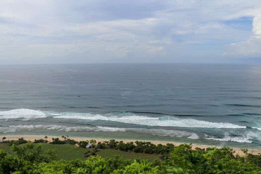 Aerial view of Nyang Nyang beach on Bali in Indonesia. A popular spot of surfers with big waves in the Indian Ocean. Fishing boats of Balinese fishermen on the sea surface. Waves break off the coast.