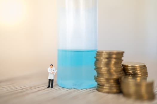 Healthcare,  Coronavirus (COVID-19) situation Business and Econony Cocept. Doctor miniature figure people with patient clipboard standing with stack of gold coins with alcohol gel sanitizer on wooden table.