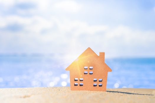 Closed up tiny home models on sand with sunlight and beach background.Investment property concept.