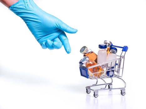 hand with blue latex glove reaching out for Medical vials with solution for injection in shopping cart, on white background. Vaccine for coronavirus concept.