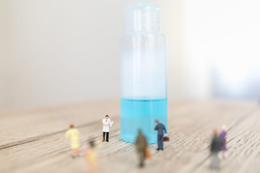 Global Healthcare, Coronavirus, Covid-19 Protection Concept. Doctor miniature figure people with patient clipboard standing with alcohol gel sanitizer with group of people on wooden table.