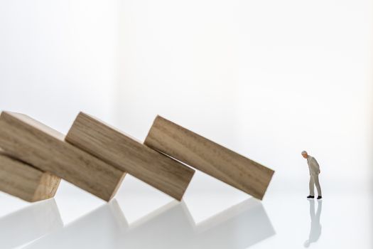 Crisis and failure in Business, Insurance and Risk Management Concept. Close up of businessman miniature figure people looking to wooden block  the collapse of fall in line, with copy space.