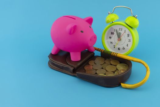 Saving for old-age and retirement concept with open purse with coins, walking stick, alarm clock and piggy bank over a blue background with copy space