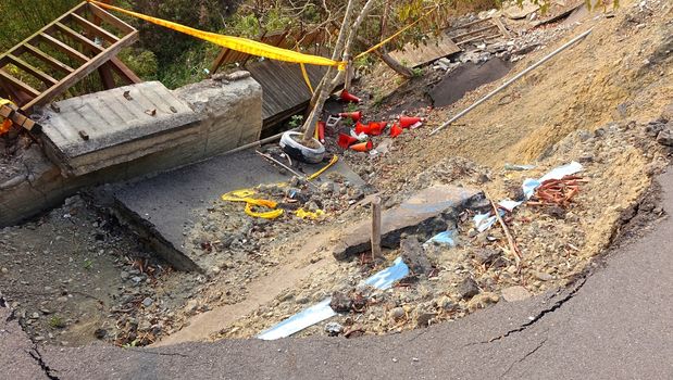 A road and built structures are damaged by a landslide
