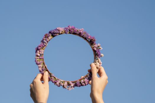 Woman holding wildflowers head crown on a blue sky.