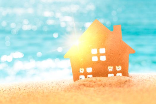 Closed up tiny home models on sand with sunlight and beach background.Investment property concept.