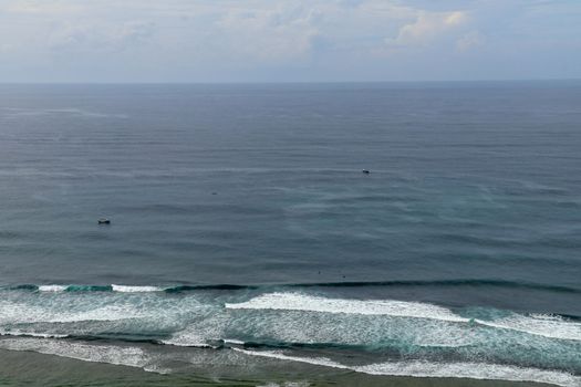 Young surfers sitting on surfboards waiting for the right wave. A young man lies on the surfboard and is spending time talking to other friends. Waves turn into sea foam as they break off the coast.