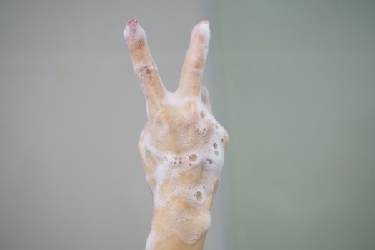 Hand with soft foam bubble from soap is showing Victory sign.