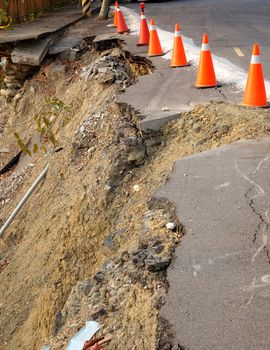 Red and white traffic cones on a  road that has been damaged by a landslide