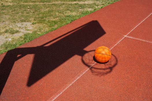 Basketball on a court placed inside the shadow of the net and goalpost in a conceptual image with copy space