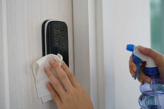 Woman hand using napkin and detergent spray cleaning doorknob for corona virus or Covid-19 protection.