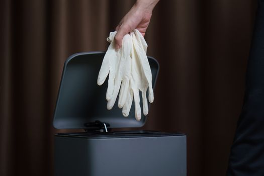 Hand putting used dirty surgical glove to a garbage bin. Mask protect dust and corona virus in trash.