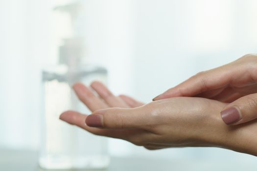 Female hands using wash hand sanitizer gel pump dispenser. Clear sanitizer in pump bottle, for killing germs, bacteria and virus.