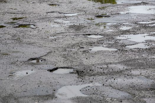 bumpy damaged road asphalt with multiple puddles after rain at summer daytime, potholes.