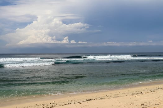 Virgin beach with fine yellow sand on Bali island. Lonely tropical paradise with Nyang Nyang beach. Azure blue sky, sunny day. Wild waves are approaching the shore in rows. Sea foam in rolling waves.