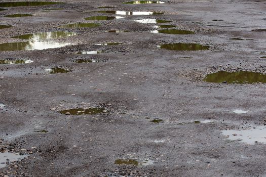 bumpy damaged road asphalt with multiple puddles after rain at summer daytime, potholes.