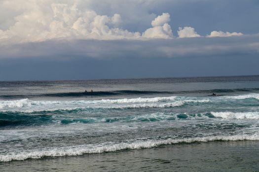 Surfers are waiting for a convenient wave on their surfboards. Tropical surfers paradise with Nyang Nyang beach on Bali island. Azure blue sky, sunny day. Wild waves are approaching the shore in rows.