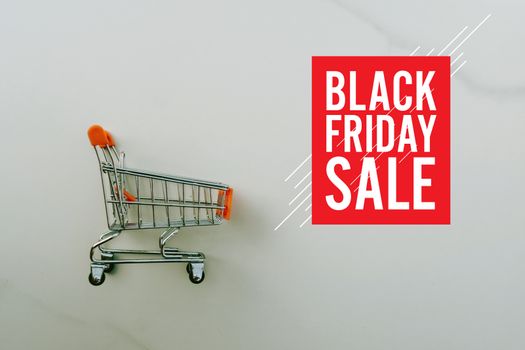 Shopping cart on marble white floor texture background with black friday sale graphic design. 