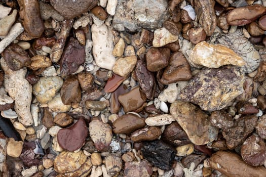 Multicolor stones of different shapes and size. Small rocks on beach sand close up.