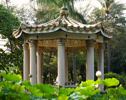 A Chinese pavilion with glazed roof tiles in the middle of a pond with water lilies