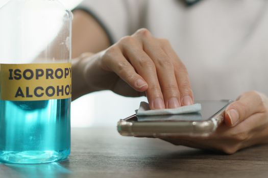 Hand pouring ethyl alcohol from bottle into a cotton piece for clean mobile phone, corona virus or Covid-19 protection.