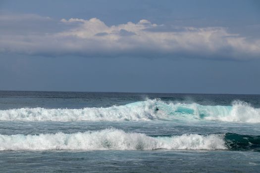 Young caucasian man surfs the ocean wave and makes a lot of splashes into the camera. Nyang Nyang Surf Spot in Bali, Indonesia. The surfer falls into the ocean waves. Man rides the wave at sunny day.