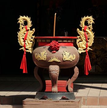 A Chinese incense burner with a large burning joss stick and two golden dragon decorations